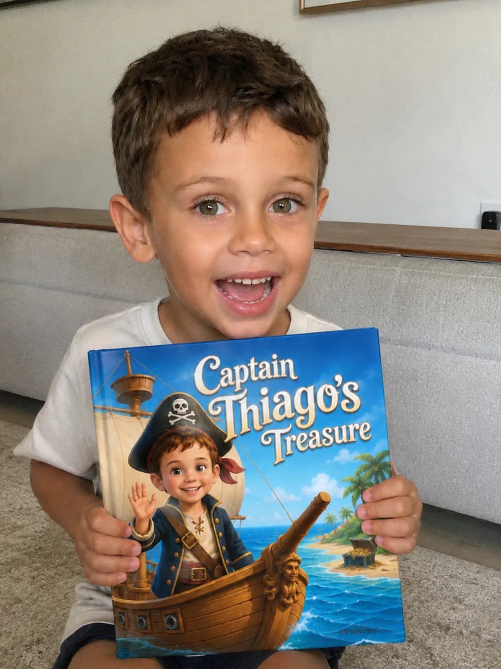 The same boy smiling, holding his finished hardcover book — his pirate hero on the cover.